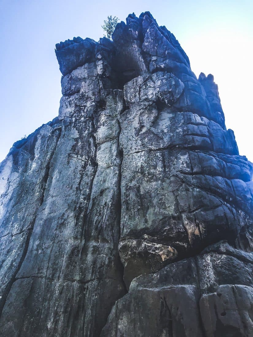 Ein hoher, zerklüfteter Felsturm von unten gesehen vor hellblauem Himmel