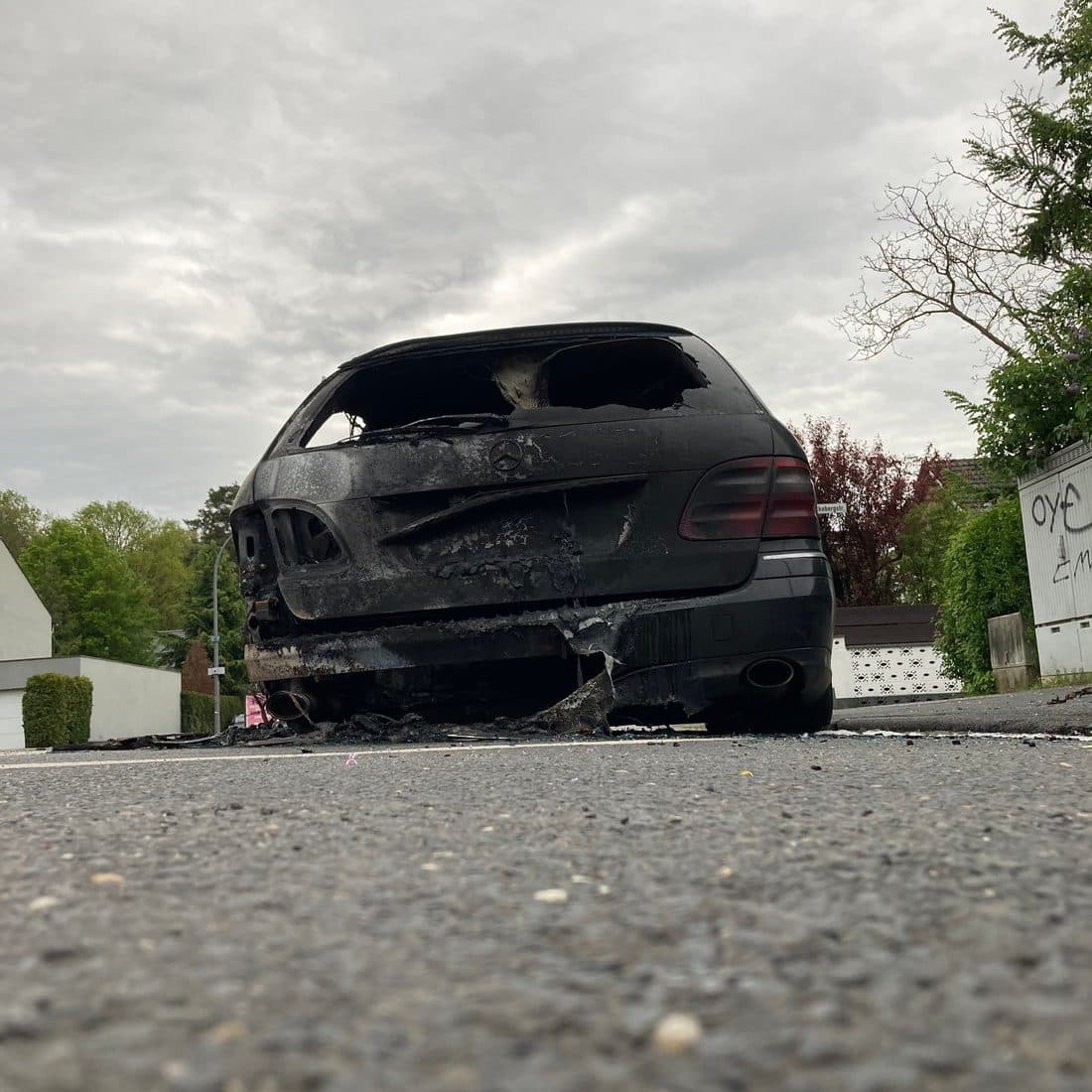 Ein ausgebranntes Auto am Straßenrand, von hinten und von unten gesehen, unter grauem Himmel