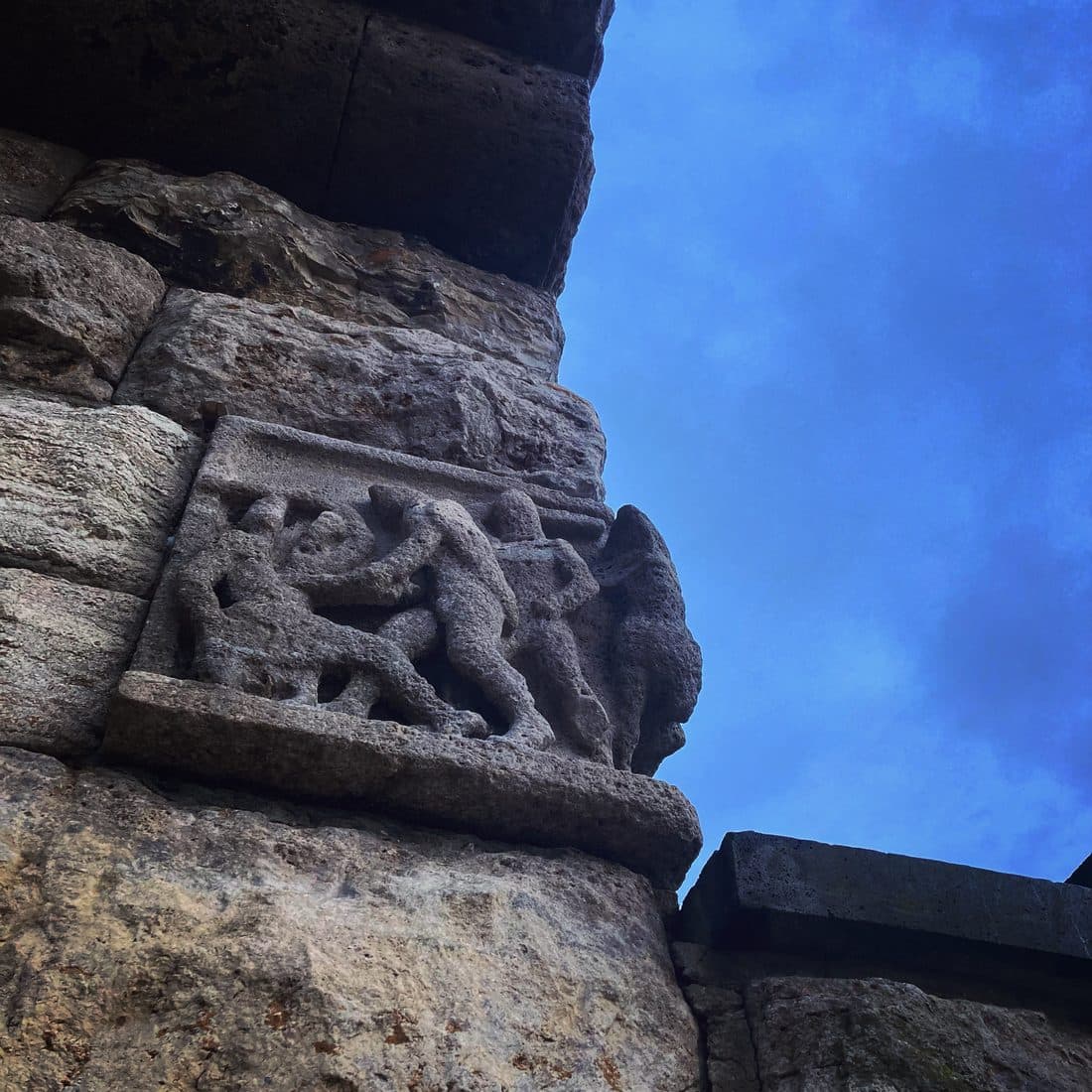 Ein Relief mit Figuren in einer Steinmauer, darüber blauer Himmel