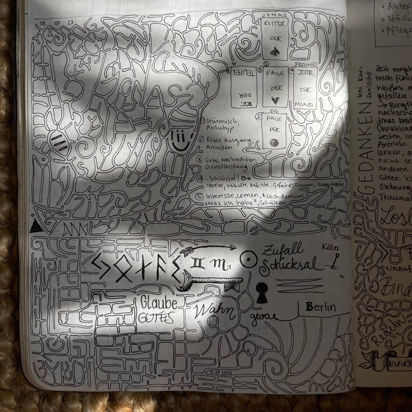 Eine Notizbuchseite voller labyrinthartiger Linien, dazwischen handgeschriebene Wörter wie Zufall, Schicksal, Glaube und Wahn