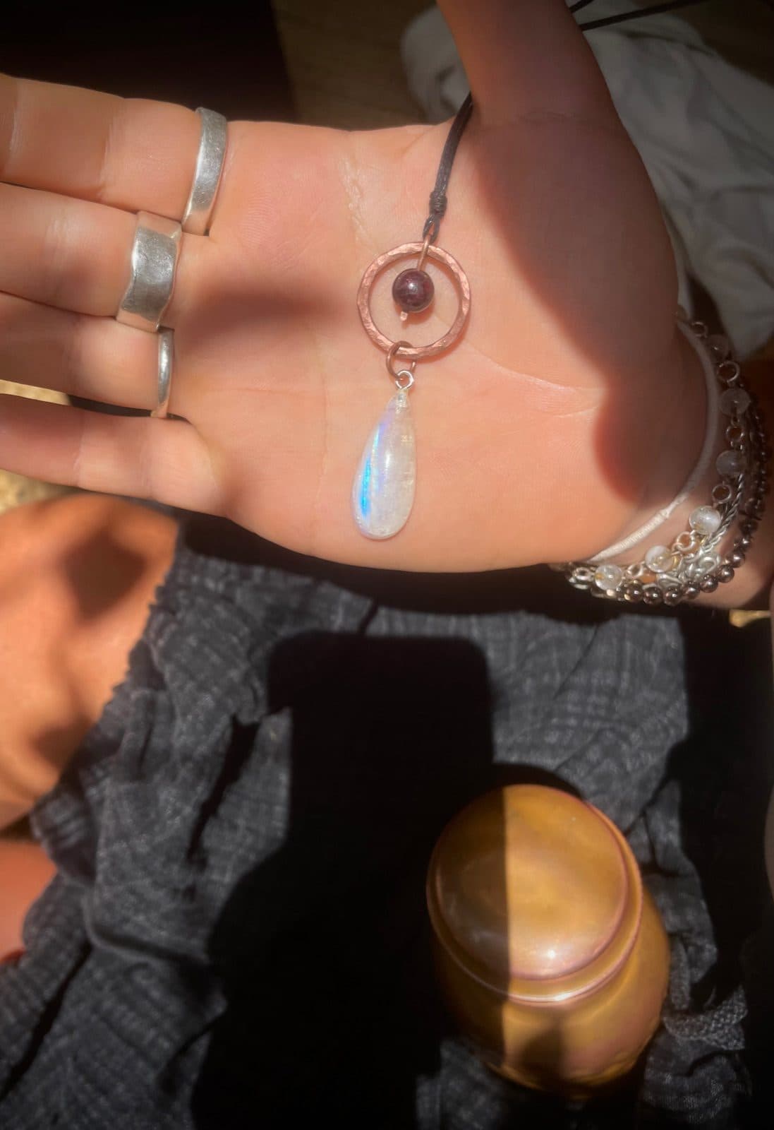 Der Anhänger liegt in einer offenen Handfläche im Sonnenlicht, der Mondsteintropfen schimmert blau